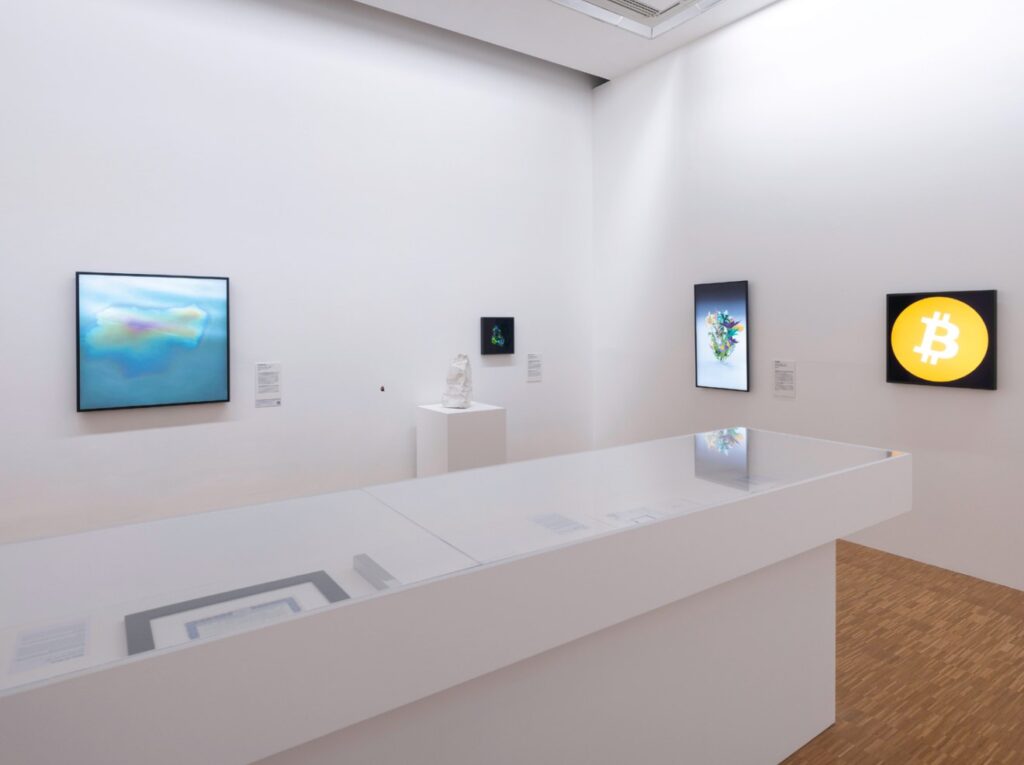 Centre Pompidou gallery room from the exhibition NFTs: Poetics of the Immaterial, with screen-based works on white walls and a long glass display case